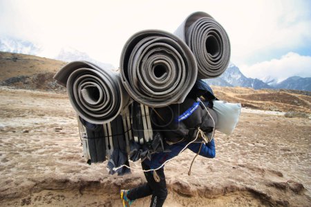 Téléchargez les photos : Sherpa Porter portant une lourde charge sur les sentiers de trek du camp de base de l'Everest en direction du village de Gorakshep, au Népal - en image libre de droit