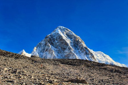 Mount Pumori at 7163 meters is seen towering over the Kala pathar hill top in the golden light of  dawn with bright blue skies in this stunning portrait like image near Gorakshep,Nepal