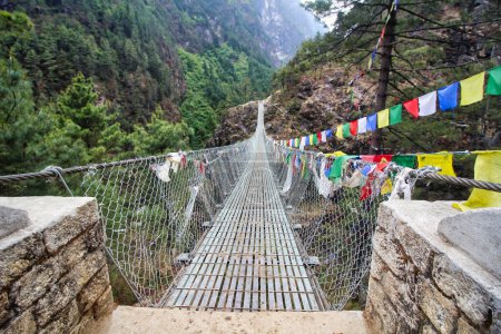 Trekkerzy na Everest Base Camp przechodzą przez stalowe mosty linowe nad strumieniami ozdobionymi flagami modlitewnymi w pobliżu Lukla, Nepal