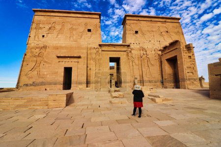 Un visitante admira los magníficos relieves murales que representan a Ptolomeo en el pilón de entrada del Templo de Isis en la Isla Philae en el lago Nasser, construido por Nectanebo y Ptolomeo Faraones cerca de Asuán, Egipto