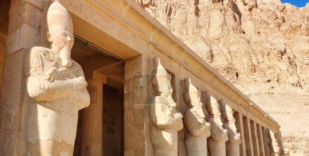 Téléchargez les photos : Statues massives de la Grande Femme Pharoah Hatchepsout avec le escroc et le fléau comme souverain de l'Egypte sculpté dans le grès dominent les colonnes extérieures du temple mortuaire près de Louxor, Egypte - en image libre de droit