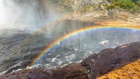 A Beautiful rainbow formed in the mists at the base of the Montmorency falls on a bright sunlit summer day  near Quebec city, the capital of Quebec province,Canada