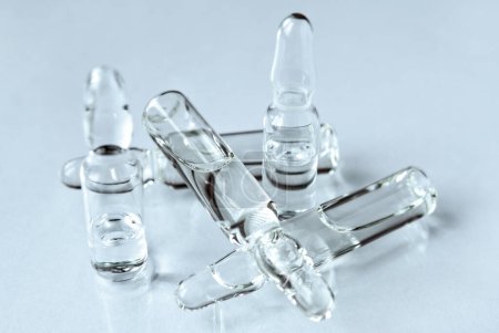 Foto de Ampollas médicas con fármaco transparente en una superficie ligera de cerca. Medicamentos y asistencia sanitaria - Imagen libre de derechos