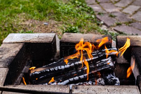 Foto de La leña se quema en la parrilla con una llama en el jardín, en verano. Área de picnic. - Imagen libre de derechos