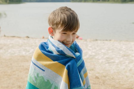 Téléchargez les photos : Un enfant est enveloppé dans une serviette après avoir nagé dans le lac. - en image libre de droit