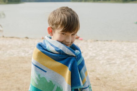 Foto de Un niño se envuelve en una toalla después de nadar en el lago. - Imagen libre de derechos