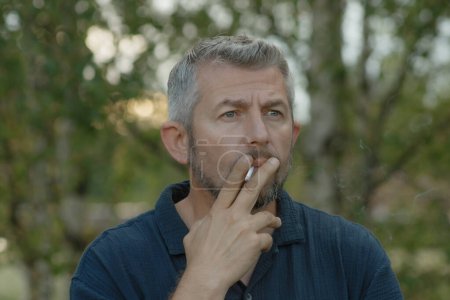 Foto de Un hombre fuma un cigarrillo afuera en la naturaleza fresca. Enfoque selectivo suave. - Imagen libre de derechos