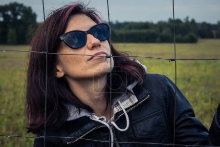 Téléchargez les photos : Une femme se tient près de la clôture et regarde. Concentration sélective douce. - en image libre de droit