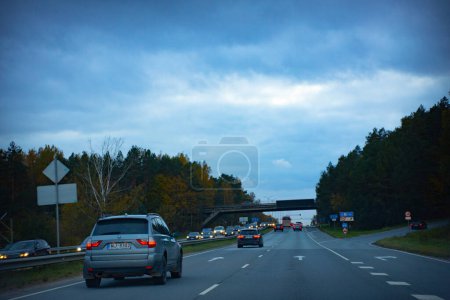 Foto de Ciudad conducir a través de coche follaje otoño en la carretera rodeada de árboles. Nubes oscuras por la noche. Viaje nocturno por el bosque de follaje otoñal. Enfoque selectivo suave. - Imagen libre de derechos