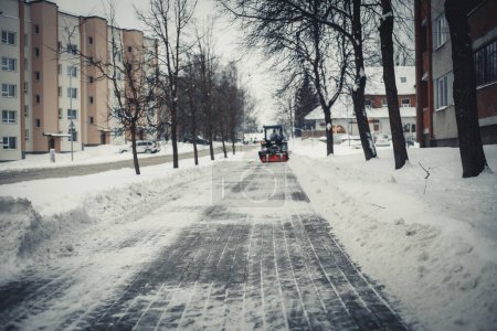 Foto de Casas de ciudad cubiertas de nieve. Y los caminos están cubiertos de nieve. El tractor limpia la carretera. - Imagen libre de derechos