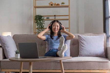 Téléchargez les photos : Portrait d'une jeune femme asiatique heureuse écoutant de la musique avec des écouteurs sans fil de l'application musicale dans un ordinateur portable. - en image libre de droit