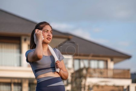 Foto de Mujer asiática cansada y sudorosa en ropa deportiva utiliza una toalla para limpiar el sudor. y tomar un descanso de correr cardio en el parque.. - Imagen libre de derechos