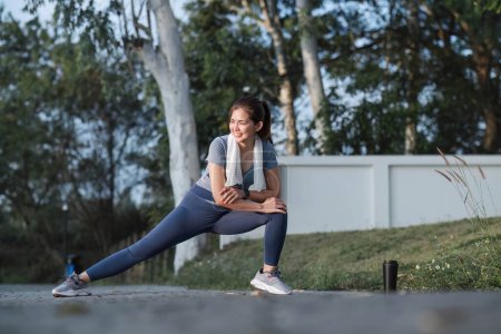 Photo for Young Asian woman exercising before a fitness session at the park in front of her house. Young healthy woman warming up outdoors She was stretching her arms and looking away.. - Royalty Free Image