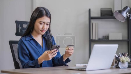 Photo for Attractive millennia Asian female holding her smartphone and credit card, using mobile banking app or online shopping app.. - Royalty Free Image
