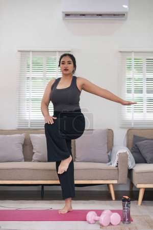 Photo for Overweight Asian woman exercising at home on a fitness mat. Beautiful Caucasian woman in casual clothes Preparing to do yoga Practice exercise in the living room. - Royalty Free Image