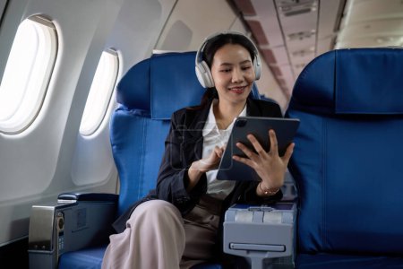 Photo for Young Asian executives are first class. Multitask with digital tablets, laptops and smartphones. Travel in style.. - Royalty Free Image