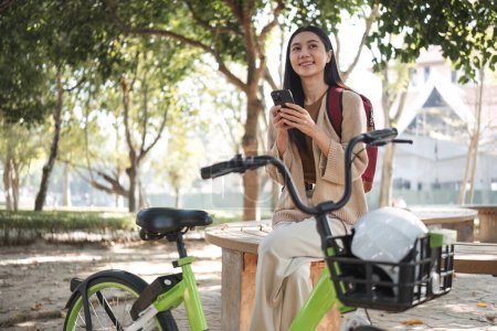 Téléchargez les photos : Une femme se repose dans le parc pour le travail et utilise les médias sociaux sur son smartphone après avoir fait du vélo dans le parc.. - en image libre de droit
