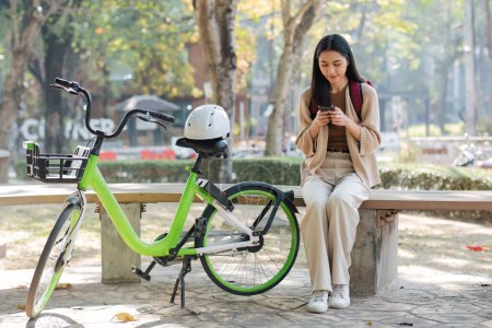 Téléchargez les photos : Une femme se repose dans le parc pour le travail et utilise les médias sociaux sur son smartphone après avoir fait du vélo dans le parc.. - en image libre de droit