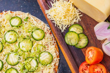 Foto de Preparación de pizza, distribución de rodajas de pepino y rodajas en pizza de pepino vegetariano, ingredientes frescos de pizza en tablero de madera. - Imagen libre de derechos