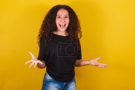 Photo for Brazilian latin american girl for afro hair, yellow background, smiling, making surprised expression with face and hands, wow, surprised - Royalty Free Image