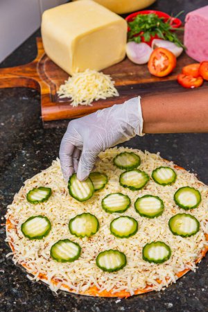Téléchargez les photos : Préparation de pizza, épandage de tranches de concombre et de tranches sur une pizza végétarienne au concombre, ingrédients de pizza fraîche sur du carton en bois. - en image libre de droit
