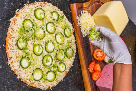 Photo for Pizza preparation, spreading cucumber slices and slices on vegetarian cucumber pizza, fresh pizza ingredients on wooden board. - Royalty Free Image