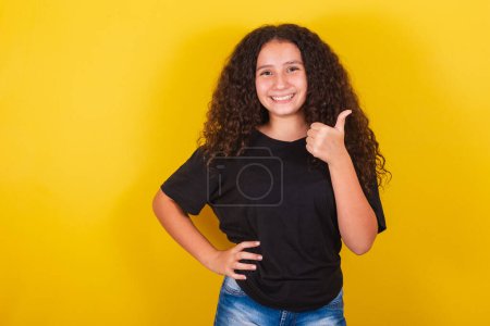 Foto de Brasileña, chica latinoamericana para cabello afro, fondo amarillo, sonriente, pulgares arriba, ok, afirmación positiva, joyería, pulgar. - Imagen libre de derechos