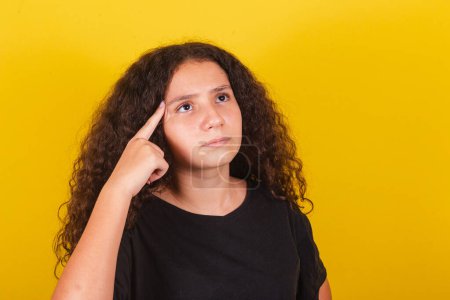 Photo for Brazilian, latin american girl, for afro hair, yellow background, expression of doubt, thinking, questioning, finger on forehead - Royalty Free Image