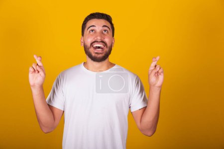 Photo for Brazilian Latin American man, fingers crossed, lucky sign, cheering, anxiety, hopeful, draw, happy, joyful, yellow background - Royalty Free Image