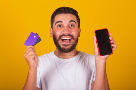 Photo for Brazilian Latin American man, Surprised and happy, showing cellphone screen and credit card, mobile phone shopping, app, internet shopping concept. - Royalty Free Image