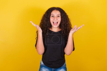 Photo for Brazilian latin american girl for afro hair, yellow background, smiling, making surprised expression with face and hands, wow, surprised - Royalty Free Image