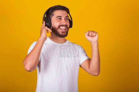 Foto de Hombre brasileño latinoamericano, feliz, con auriculares musicales, disfrutando de un sonido, feliz escuchando música. Fondo amarillo - Imagen libre de derechos