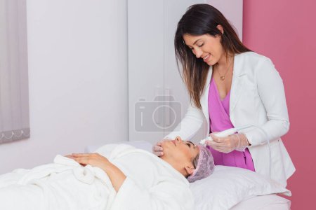 Foto de Esteticista doctor, mujer aplicando chorro de plasma facial en paciente, aplicación de procedimiento estético, rejuvenecimiento. - Imagen libre de derechos