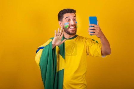 Photo for Brazilian latin american man cheering for brazil at world cup 2022 on video call talking with friends remotely, cellphone, holding cellphone, communication, technology - Royalty Free Image