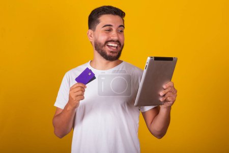 Téléchargez les photos : Brésilien latino-américain homme, surpris et heureux, tenant tablette et carte de crédit, faire des achats via App ou Internet. - en image libre de droit