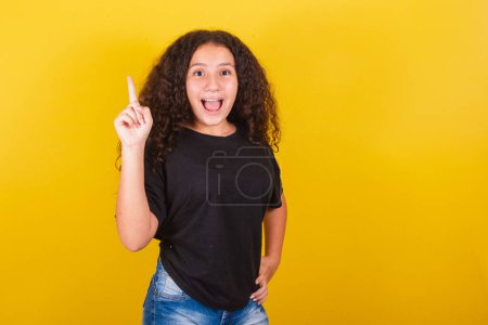 Photo for Brazilian Latin American girl for Afro hair, yellow background, expression of idea, creative, suggestion, idea, I, indication of knowing the answer, index finger raised. - Royalty Free Image