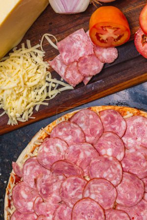 Photo for Pre-baked pepperoni pizza with fresh pizza ingredients on wooden board. - Royalty Free Image