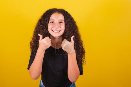 Photo for Brazilian, latin american girl for afro hair, yellow background, smiling, thumbs up, ok, positive affirmation, jewelry, thumb. - Royalty Free Image