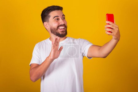 Photo for Brazilian Latin American man, Taking selfie with cell phone, on video call, talking, smiling, photographing. Yellow background. - Royalty Free Image