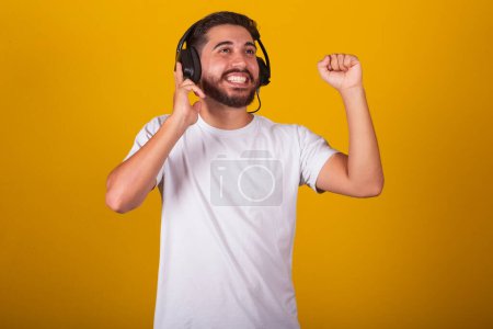 Foto de Hombre brasileño latinoamericano, feliz, con auriculares musicales, disfrutando de un sonido, feliz escuchando música. Fondo amarillo - Imagen libre de derechos