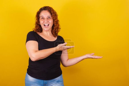 Photo for Caucasian, Brazilian, Latin American woman, curly hair, curls, yellow background, hands and fingers pointing to the side, negative space for advertising, advertisement, texts, advertisements, products, indicating, suggesting. - Royalty Free Image