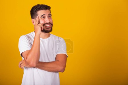 Photo for Brazilian Latin American man with hands on forehead and chin representing thought, pensive, doubt, questioning, decision, uncertainty, yellow background - Royalty Free Image
