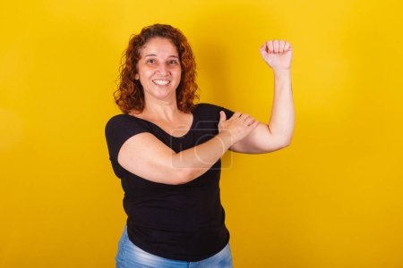 Photo for Caucasian, Brazilian, Latin American woman, curly hair, curls, yellow background, hand on biceps, empowerment, feminism, women power, female power, smiling, optimistic, confident. - Royalty Free Image