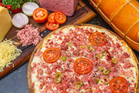 Foto de Deliciosa pizza mixta de queso y jamón, lista, pizza horneada, pizza casera. junto a tabla de madera con ingredientes - Imagen libre de derechos