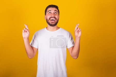 Foto de Hombre latinoamericano brasileño, dedos cruzados, signo de la suerte, animar, ansiedad, esperanzado, dibujar, feliz, alegre, fondo amarillo - Imagen libre de derechos