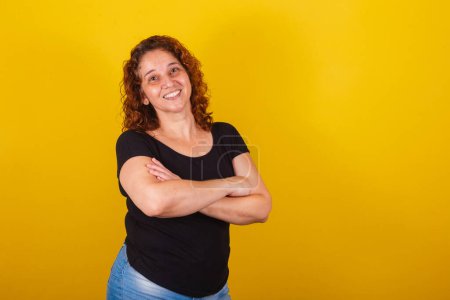 Photo for Caucasian, Brazilian, Latin American woman, curly hair, curls, yellow background, arms crossed, smiling happy and cheerful, confident, optimistic. - Royalty Free Image