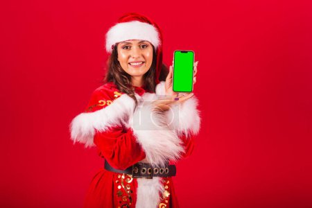 Téléchargez les photos : Femme brésilienne vêtue de vêtements de Noël, le Père Noël. tenant smartphone avec écran vert en chroma. - en image libre de droit