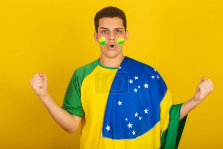Foto de Joven aficionado al fútbol brasileño. vestido de verde, gol gritando con bandera de Brasil. - Imagen libre de derechos