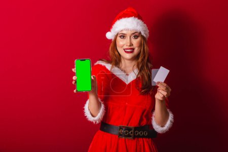 Téléchargez les photos : Belle femme rousse brésilienne, vêtue de vêtements de Noël, le Père Noël. tenant cartes de crédit et smartphone avec écran vert en chroma. - en image libre de droit