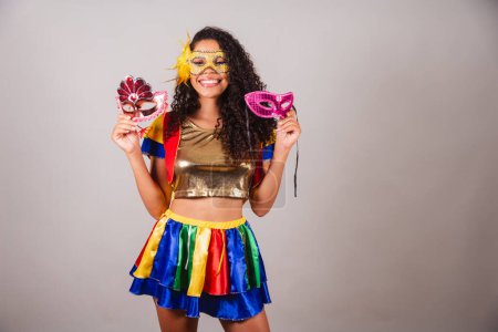 Foto de Hermosa mujer brasileña negra, con ropa frevo, carnaval. Usando una máscara, sosteniendo máscaras de carnaval, invitando a la gente a la fiesta. - Imagen libre de derechos